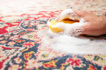 Male hand holding a yellow sponge, on a natural fiber rug with white foam, abstract texture, soft...