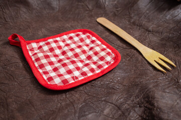 Checkered pot holder and wooden fork on genuine brown leather background, minimal backdrop