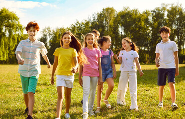 Happy children friends standing together outdoors, having fun and smiling in park on holidays enjoying spending time in summer camp. Portrait of a kids walking in natureand having weekend activity