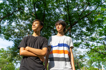 Two joyful teenage boys looking at the camera in the summer park against the blue sky.