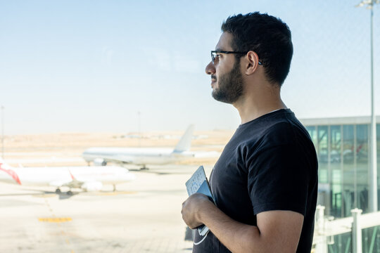 Young arab male holding his passport at the airport ready for new adventure with airplane in the background