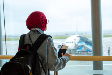 Arabic muslim female at the airport holding her passport and looking at airplane