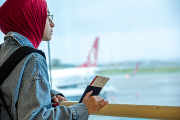 Arabic muslim female at the airport holding her passport and looking at airplane