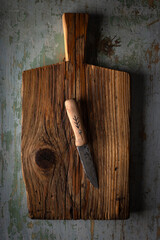 Small knife with wooden handle lying on an old cutting board on rusty aged table