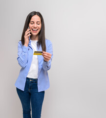 Smiling young businesswoman holding credit card and talking over smart phone on white background