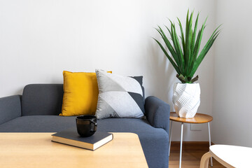 White and yellow pillows on a grey sofa with coffee table in Scandinavian living room interior.