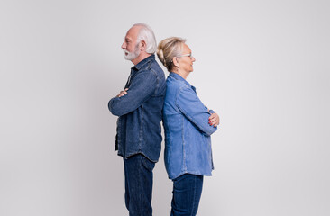 Side view of senior couple with arms crossed standing back to back and ignoring on white background