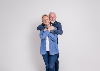 Portrait of romantic mature husband embracing wife from behind while standing over white background
