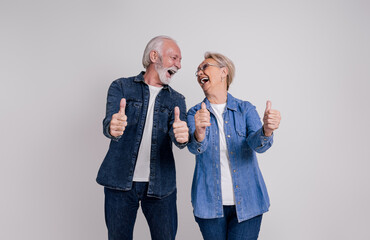Happy senior couple looking at each other and shouting while gesturing thumbs up on white background