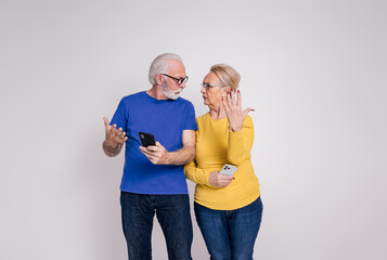 Frustrated senior couple with smart phones gesturing and arguing with each other on white background