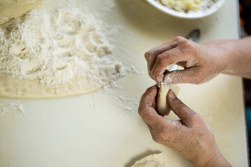 A woman makes dumplings and ravioli from flour and dough with her hands.
