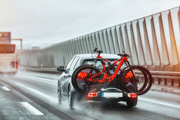A car with a rack of full-suspension mountain bikes mounted on the trunk travels on the highway for...
