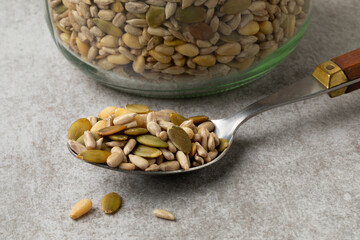 Mixture of dried salad seeds on a spoon in front of a glass jar close up  