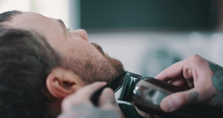 Beard, shave or grooming with the hands of a barber and man as a customer for luxury or professional service. Face, salon or hairdresser and a person shaving a client with an electric razor machine