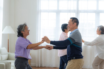 Obraz premium Asian Older male and females people dance with their partners on a dancing floor in living space. Happy older couple performing get exercise. Joyful carefree retired senior friends enjoying relaxation