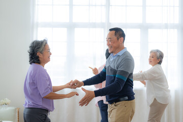 Obraz premium Asian Older male and females people dance with their partners on a dancing floor in living space. Happy older couple performing get exercise. Joyful carefree retired senior friends enjoying relaxation