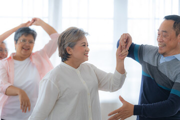 Obraz premium Asian Older male and females people dance with their partners on a dancing floor in living space. Happy older couple performing get exercise. Joyful carefree retired senior friends enjoying relaxation