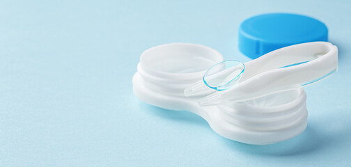 Contact lens on tweezer with container on light blue background - obrazy, fototapety, plakaty