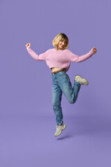 Happy pretty gen z blonde young woman, cute smiling hipster girl with short blond hair wearing jeans, sneakers and pink sweater dancing jumping isolated on purple background. Full length shot