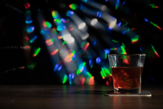 Glass of whiskey on the bar in front of the blur image Christmas background. Festive abstract background with bokeh defocused lights and stars
