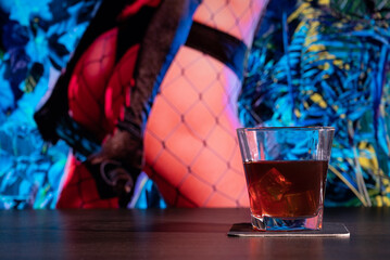 Glass of whiskey on the bar in front of the blur image Sexy woman in Thong. Lady with a leather whip. BDSM toys for role-playing sexual games with domination and submission