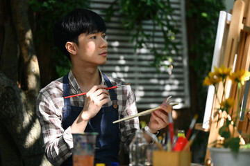 Talented asian male Artist wearing apron creating artwork at outdoor. Creative hobby concept.