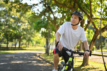 Active retired man in helmet riding bicycle in park on sunny summer day