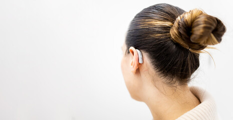 An unrecognizable woman stands on a white background trying on a BTE hearing aid. Sound...