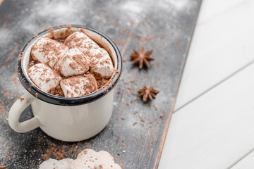 Homemade spicy hot chocolate drink with white marshmallows in enamel cup on wooden table with cinnamon stick, cookies and star anise