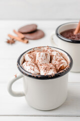 Homemade spicy hot chocolate drink with marshmallows in enamel cup on white wooden table with cinnamon stick, cookies and star anise