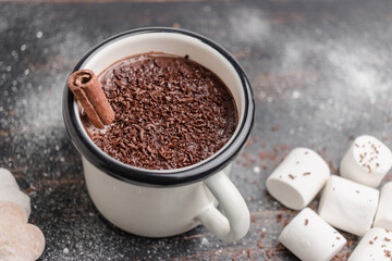 Homemade spicy hot chocolate drink with cinnamon stick, grated chocolate in enamel mug on wooden table with cookies, white marshmallows and star anise
