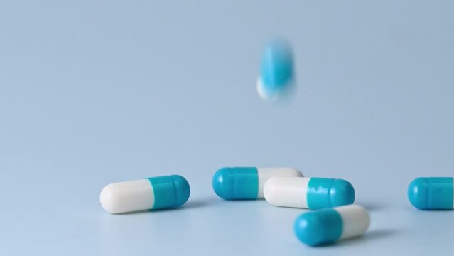 Falling blue and white medicine pill capsules on blue background close-up. Slow motion
