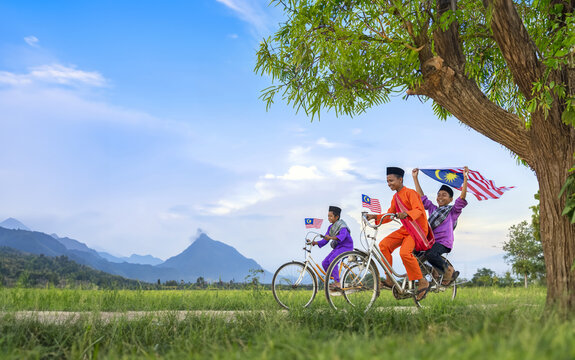 independence Day concept - Two happy young local boy riding old bicycle at paddy field holding a Malaysian flag