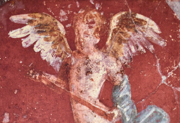 Fresco winged cupid on red background in a Domus of the ancient Pompeii, the ancient Roman city of Pompeii destroyed by the eruption of Volcano Vesuvius in 79 BC - 693904964