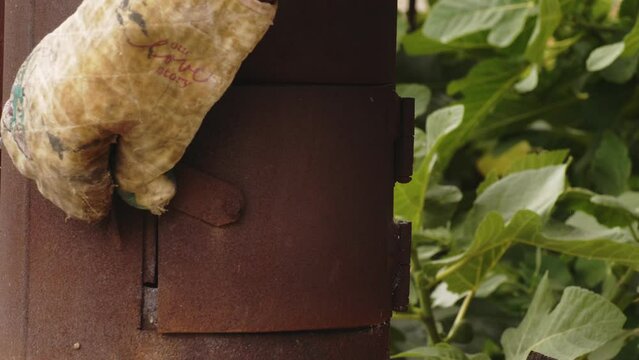 A hand in a mitten throws firewood into the firebox of an outdoor barbecue