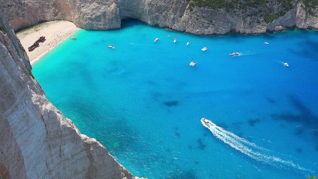 Panoramic view of rocky Navagio Beach or Shipwreck Beach. Ships floating turquoise Ionian Sea. Tourists relaxing, sunbathing on sand and enjoying amazing nature of lagoon on Zakynthos island, Greece