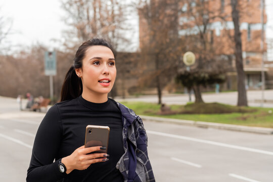 athlete girl. a girl in a black sweater runs through the city center with Rus on her hand and a phone, against the backdrop of a daytime city