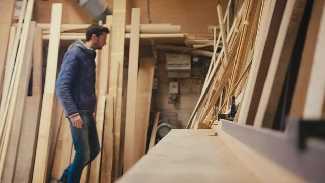 Male carpenter working in woodwork workshop choosing wood for project - shot in slow motion