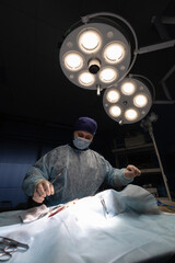 Vertical. A surgeon in the operating room during an operation on a patient. A handsome surgeon in a dark operating room operates in the light of an operating lamp. Surgeon at operation.