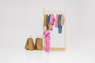 A child, a little girl, stands near the closet, chooses clothes against a light background. Dressing room with clothes on hangers. Wardrobe of children's and stylish clothes. Montessori wardrobe.