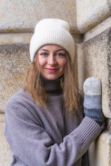 Portrait of a young woman in a knitted woolen hat and mittens. Standing near the wall