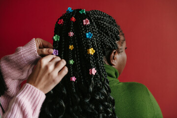 Close-up rear view of hairdresser putting on colorful clips on braided hair of African woman 