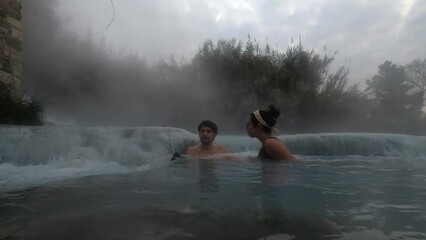 Couple relaxing and talking on Terme di Saturnia hot springs in Italy at sunrise