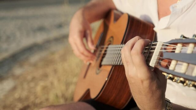 Close-up men hands playing on classic guitar . Guitarist plays the guitar in the park. Man plays guitar outdoors. Musician plays a classical guitar in the park in the summer