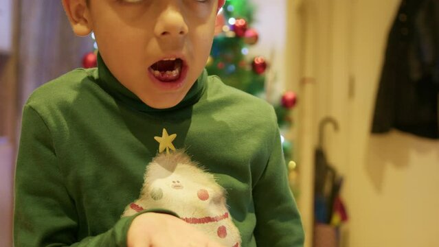 Cute boy holding his extracted milk tooth in the hand in front of the Christmas tree. High quality 4k footage
