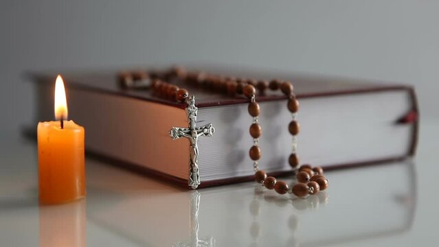 Bible, rosary and burning candle on a light background. Place of prayer for an Orthodox person.
