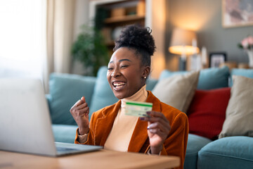 Enthusiastic charming black woman feeling excited using laptop and holding credit card satisfied with online payment possibilities, rejoicing approved loan. - obrazy, fototapety, plakaty