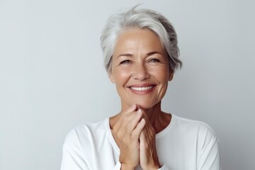 Portrait of beautiful mature woman with snow-white smile, gray hair on gray background. Middle-aged lady in light clothes, happy pensioner looking at the camera. Beauty, skin care concept
