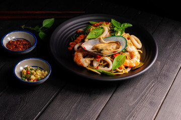Seafood drunken spaghetti with shrimp squid clams chili, and basil. Thai food. Healthy Asian in a plate on a black background table. Top view.