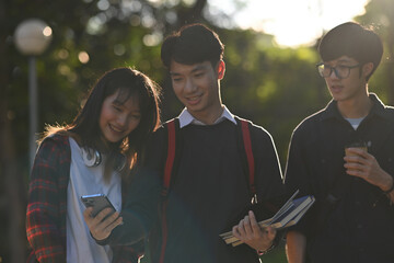 Backlit photograph of A group of Asian college students looking at a mobile phone together while...
